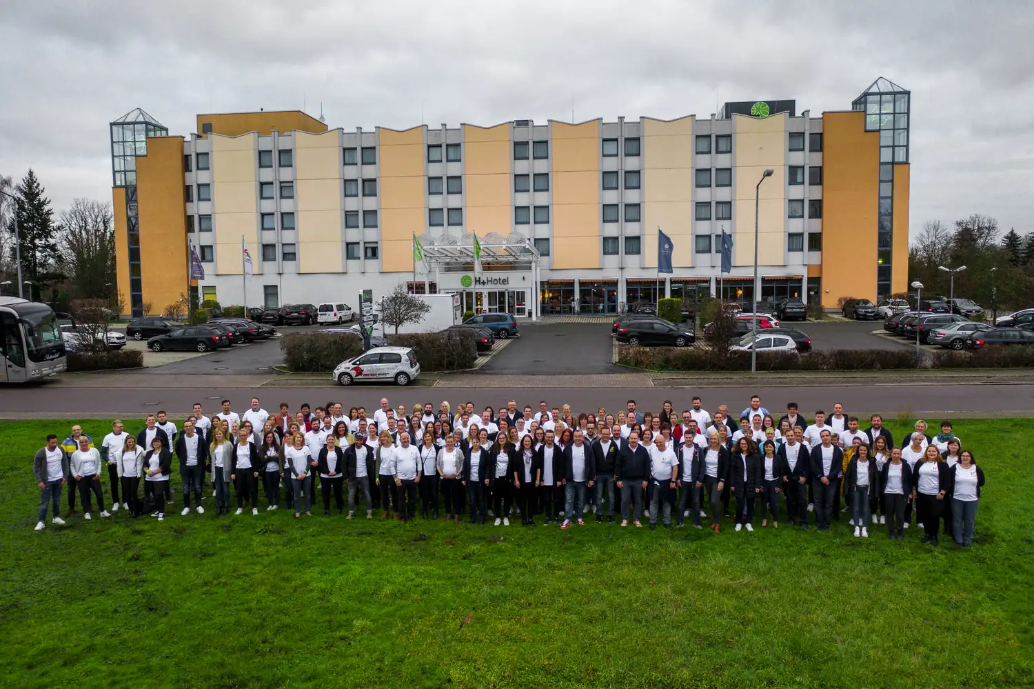 Luftaufnahme eines Hotels mit einer großen Gruppe Menschen auf der Wiese davor