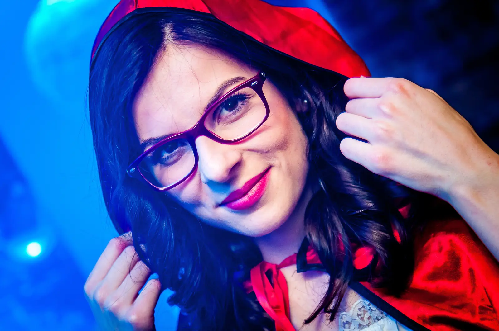 Frau mit roter Kapuze und Brille lächelt in blauem Licht