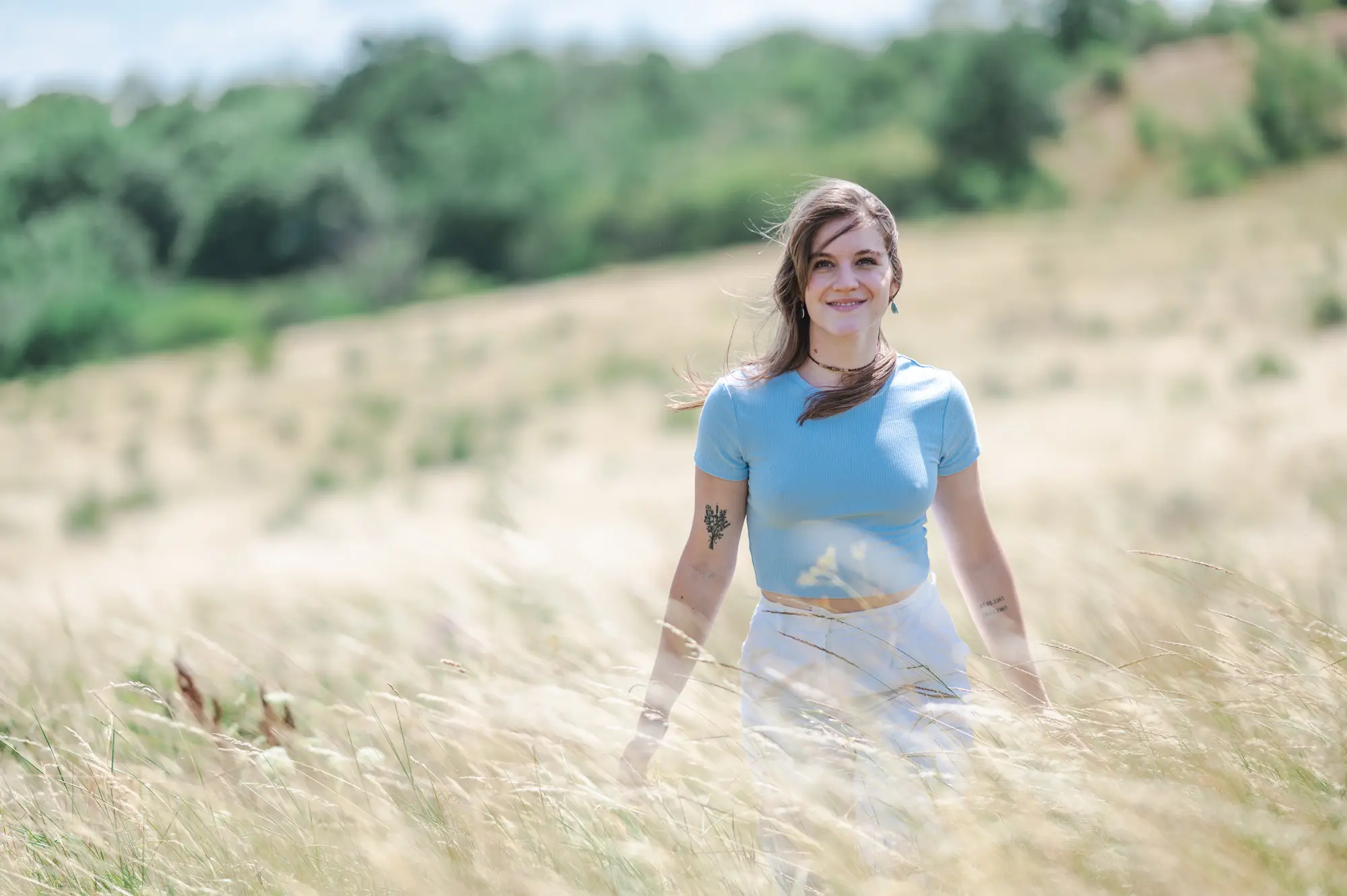 Frau in hellblauem Oberteil im hohen Gras auf einem Feld