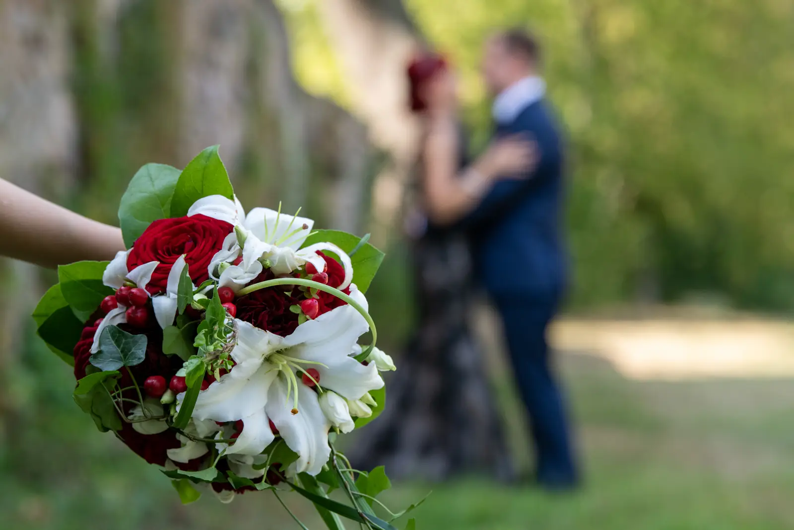 Brautstrauß mit roten und weißen Blumen, dahinter ein Paar