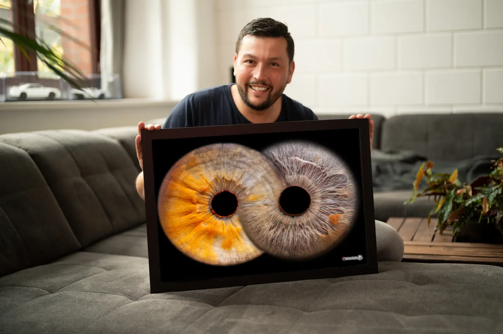 Mann hält einen gerahmten Irisfotografie-Druck mit zwei ineinander verschlungenen Augen