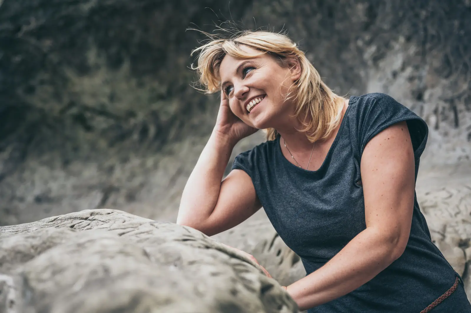 Lachende Frau lehnt an einem Felsen