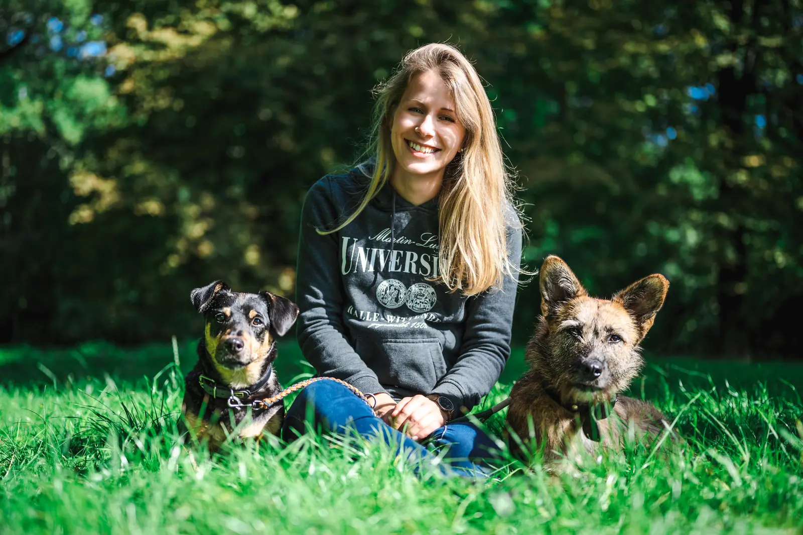 Frau sitzt mit zwei Hunden im Gras