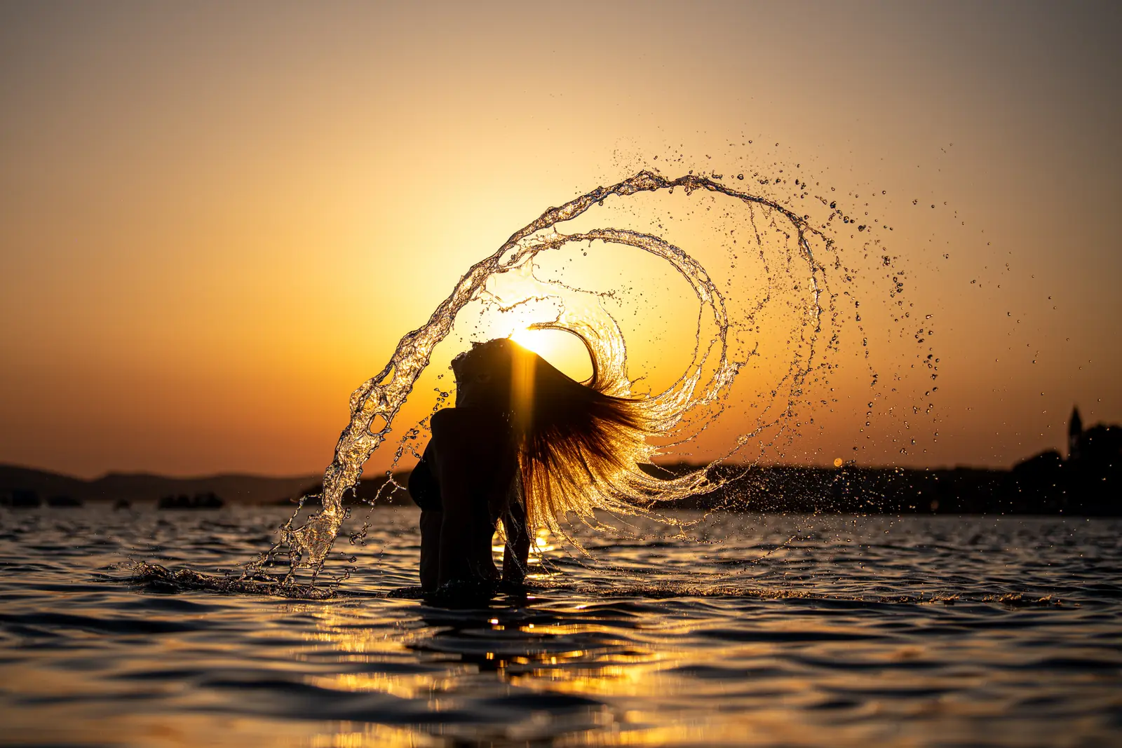 Frau schleudert im Sonnenuntergang Wasser aus ihren Haaren