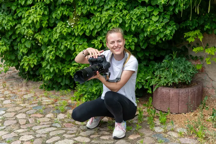Fotografin mit Kamera vor einer grünen Hecke