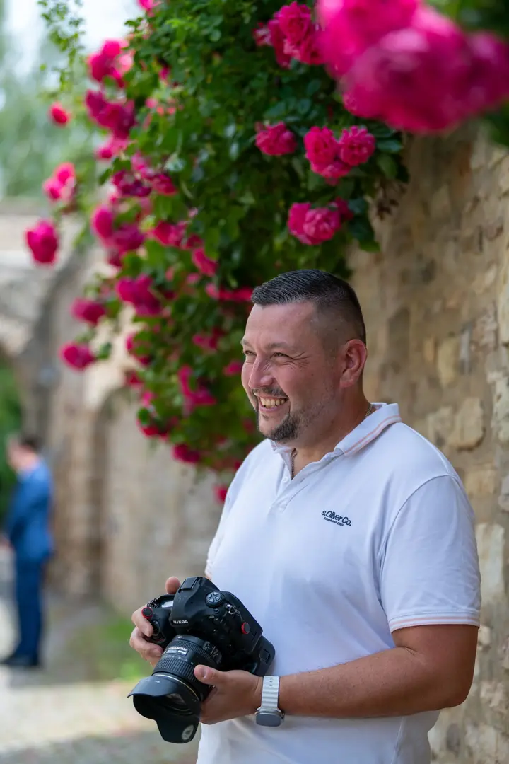 Fotograf lächelnd mit Kamera vor blühenden Rosen